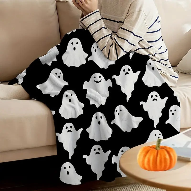 Person wrapped in the cute ghost flannel throw blanket on a cream sofa beside a pumpkin