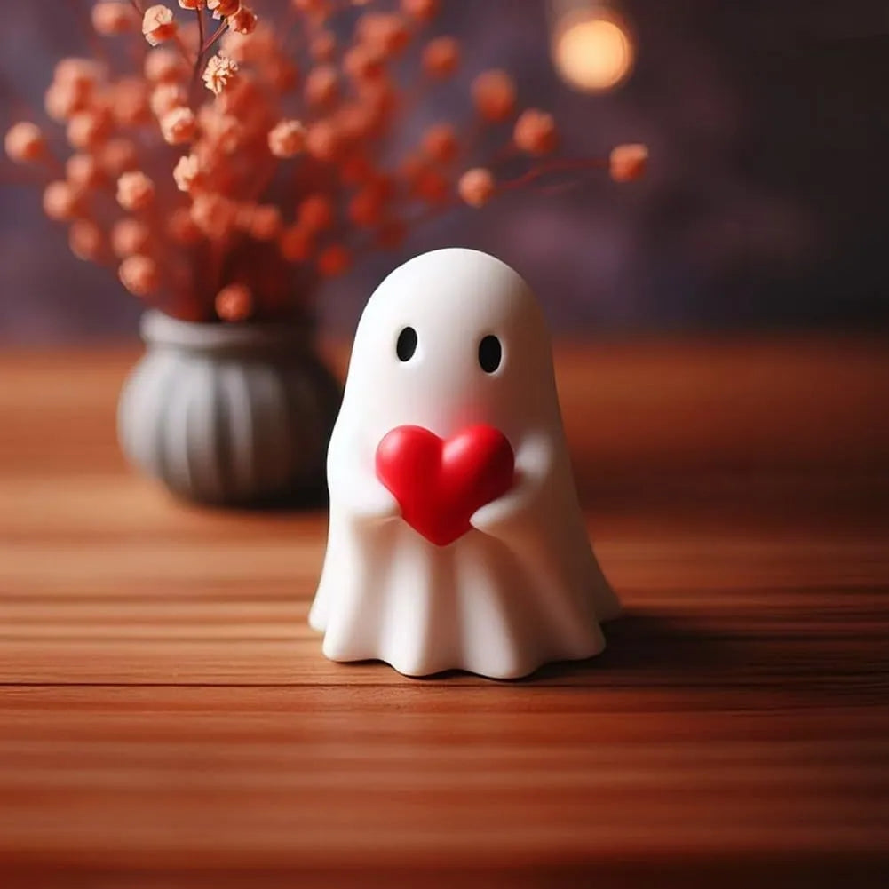 White ghost figurine holding a red heart on a wooden table beside dried flowers