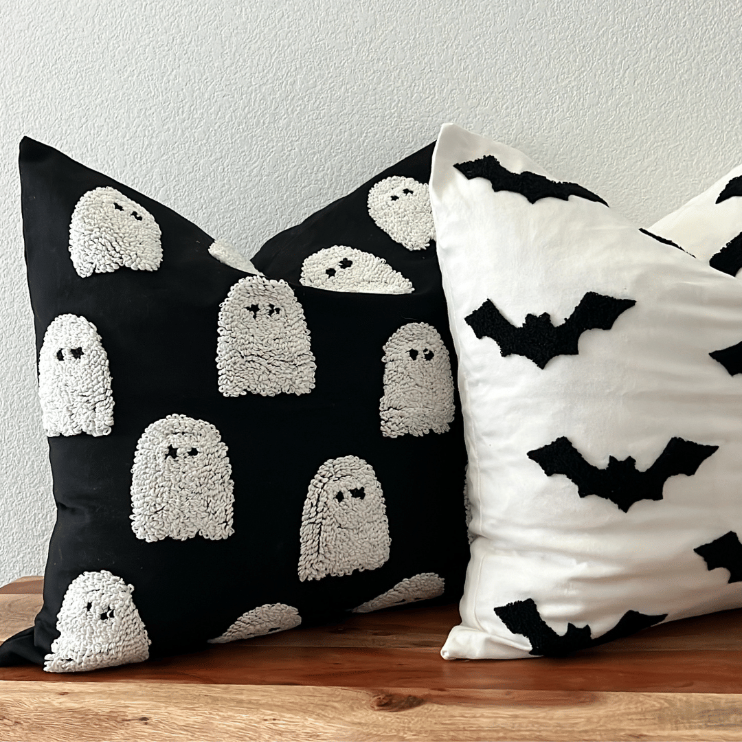 Tufted ghost pillow cover in black beside the cream tufted bat pillow cover on a wooden bench