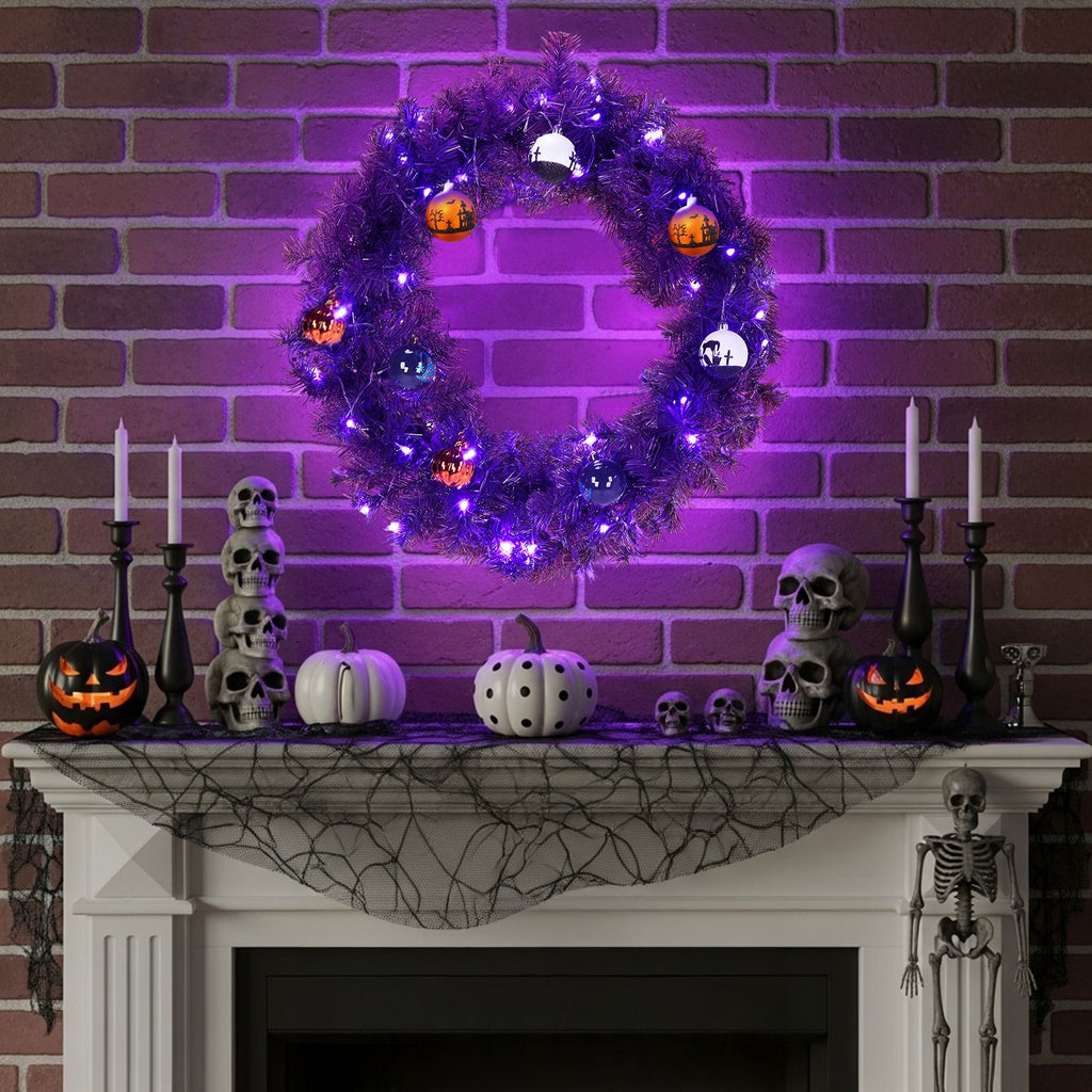 Lit purple Halloween wreath above a mantel styled with skulls and black candlesticks