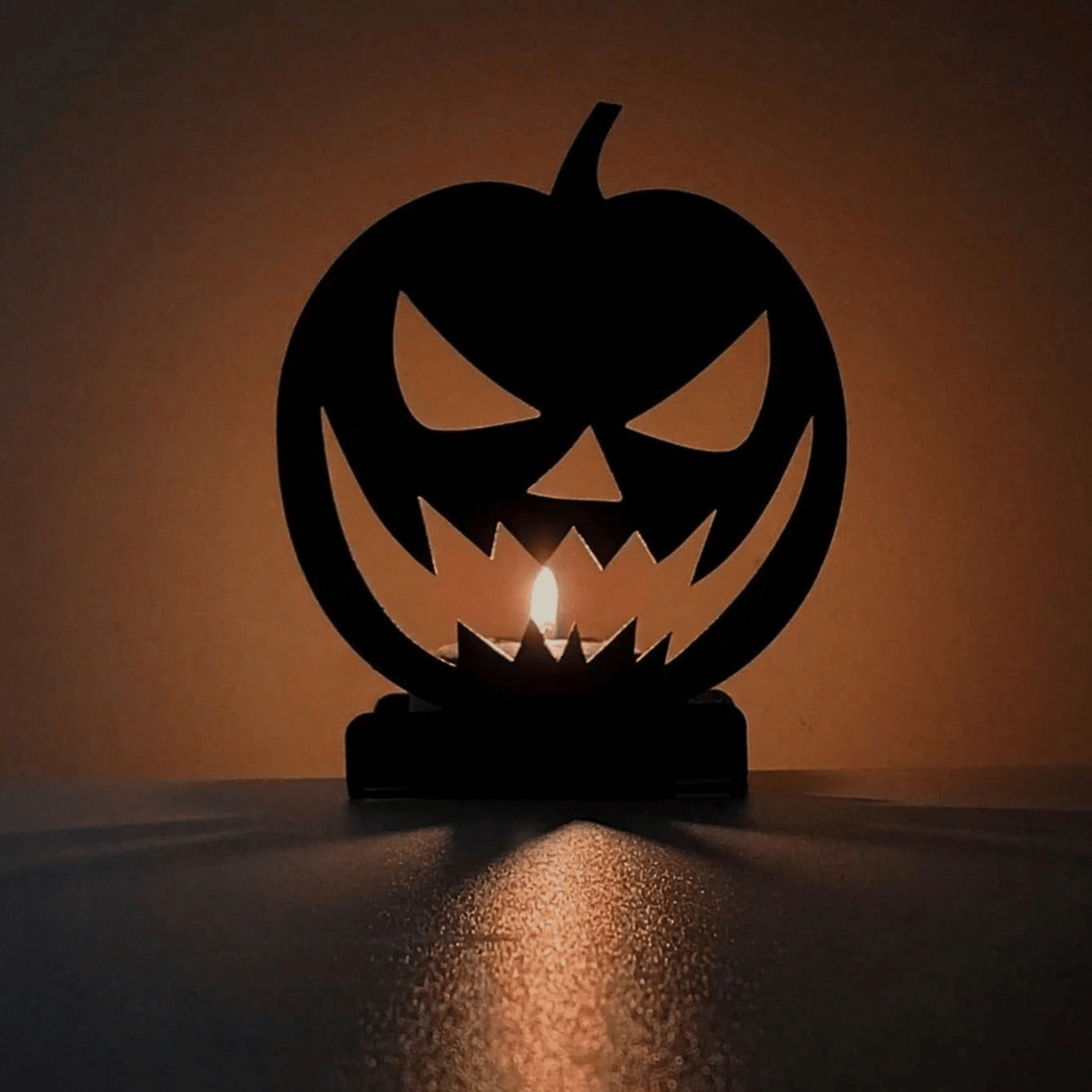 Close-up of the lit jack-o'-lantern silhouette with a tealight glowing through the grin