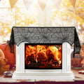 Black lace spiderweb mantel scarf draped over a white fireplace with a fire lit and pumpkins alongside