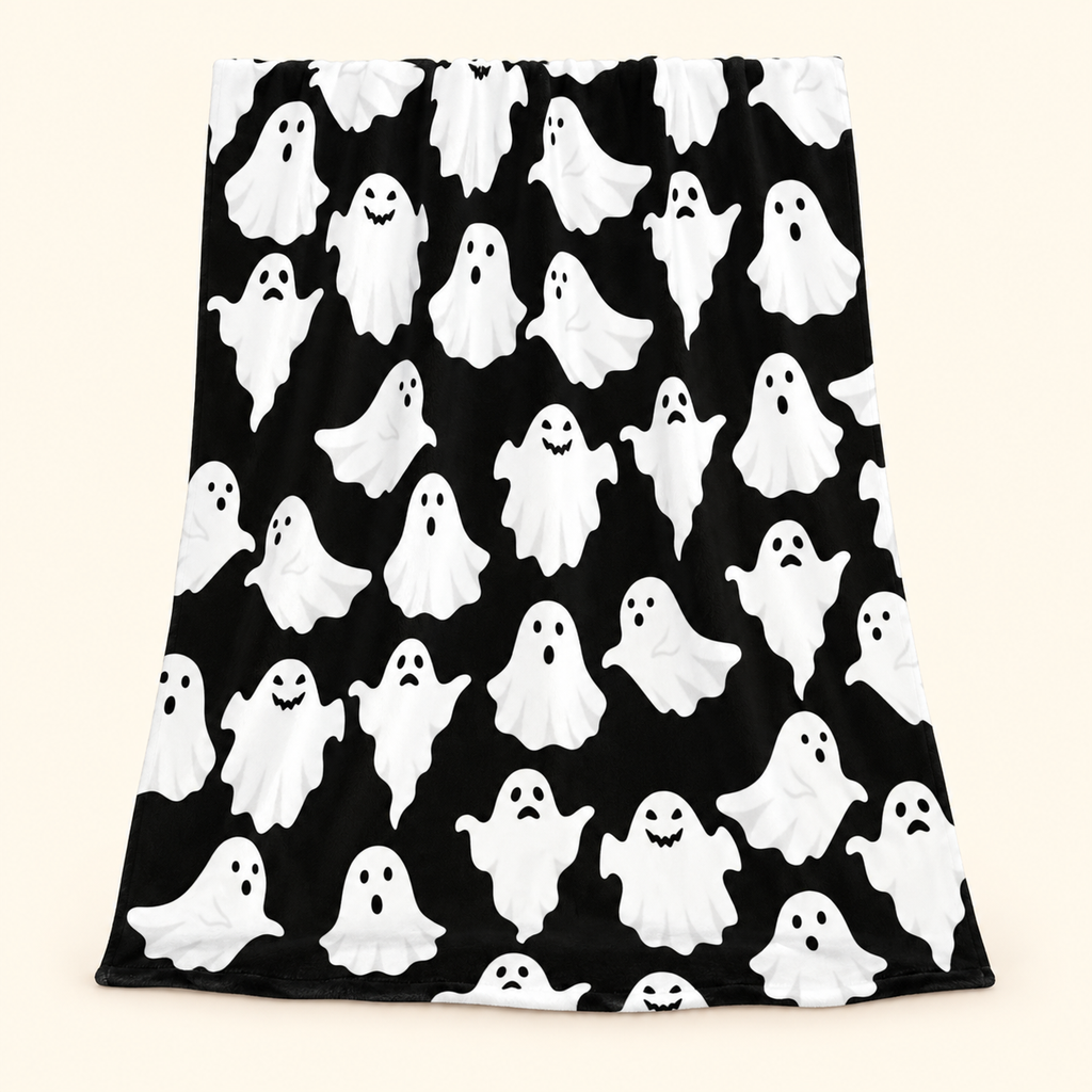Black flannel throw blanket with white cartoon ghost print against a warm ivory background